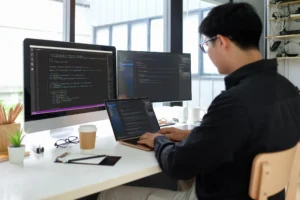 Software developer coding on multiple screens in a modern office, showcasing custom web development and software engineering services